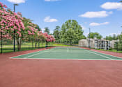Thumbnail 6 of 15 - A tennis court surrounded by trees with pink flowers.