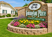 Thumbnail 1 of 22 - A sign for Kensington Place Apartments is surrounded by flowers and greenery.