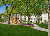 Thumbnail 6 of 22 - A playground with a yellow slide is surrounded by green trees and a grassy area.