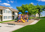 Thumbnail 4 of 22 - A playground with a slide and a swing set in front of apartment buildings.