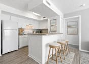Thumbnail 14 of 21 - A kitchen with white appliances and a bar area with stools.