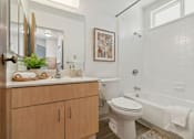 Thumbnail 16 of 16 - A bathroom with a white toilet, a white tub, and a wooden cabinet.