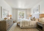 Thumbnail 12 of 16 - A bedroom with a bed, nightstand, and a window with curtains.