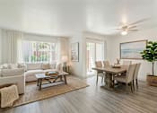 Thumbnail 8 of 16 - A living room with a white couch, a wooden coffee table, and a dining table with chairs.
