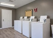 Thumbnail 3 of 13 - Three white washing machines are lined up in a laundry room at Arbors at Hickory Creek Apartments , University Park