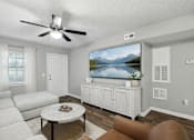 Thumbnail 15 of 23 - A living room with a white couch, a coffee table, and a television displaying a mountain landscape.