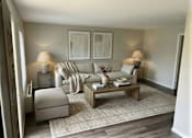 Thumbnail 10 of 14 - A living room with a grey sofa, a white armchair, a wooden coffee table, and two lamps.