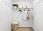 Thumbnail 18 of 21 - A white closet with clothes hanging and a basket on the floor.