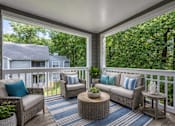 Thumbnail 12 of 26 - Covered balcony with wicker furniture and greenery views at Delta Crossing Apartments, Charlotte, NC 28212