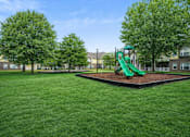 Thumbnail 14 of 25 - A playground with a green slide in the middle of a grassy area.