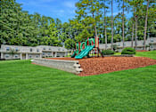 Thumbnail 6 of 22 - A playground with a green slide in the middle of a grassy area.