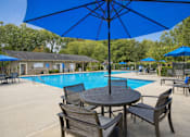 Thumbnail 4 of 15 - A blue umbrella is above a round table with chairs around it.