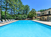 Thumbnail 8 of 22 - A large blue swimming pool surrounded by trees and lounge chairs.
