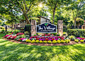 Thumbnail 1 of 15 - A sign for The Village Apartment Homes is surrounded by flowers and greenery.
