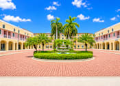 Thumbnail 1 of 10 - A courtyard with a fountain surrounded by palm trees and buildings.