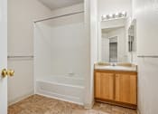 Thumbnail 21 of 36 - A white bathroom with a wooden cabinet and a white tub.