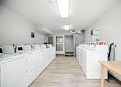 Thumbnail 4 of 8 - A clean, white-walled room with a row of white appliances and a wooden table.