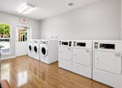 Thumbnail 14 of 24 - A row of white front load washing machines in a laundromat.