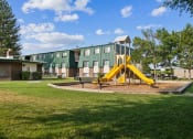 Thumbnail 21 of 35 - a playground with a yellow swing set in front of a building