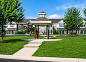 Thumbnail 2 of 16 - A gazebo-like structure sits in the middle of a grassy area in front of apartment buildings.