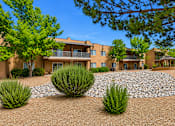 Thumbnail 5 of 24 - A building with a brown facade surrounded by greenery and a gravel area.