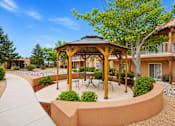 Thumbnail 2 of 24 - A gazebo with a table and chairs is surrounded by bushes and trees.