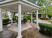 Thumbnail 17 of 22 - A white gazebo with a table and chairs is surrounded by columns and bushes.