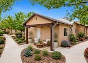 Thumbnail 6 of 24 - A small house with a porch surrounded by a garden.