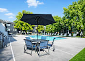Thumbnail 3 of 12 - A black umbrella is above a round table with four chairs around it.
