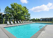 Thumbnail 2 of 12 - A swimming pool surrounded by trees and chairs.