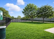 Thumbnail 5 of 8 - A green grassy area with a fence and trees in the background.