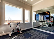Thumbnail 16 of 25 - A room with a stationary bike and a TV showing a gym workout.