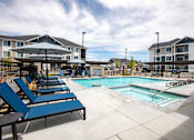 Thumbnail 11 of 25 - A pool area with sun loungers and a building in the background.