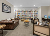 Thumbnail 7 of 13 - A living room with a brown leather couch, a coffee table, and a bookshelf filled with books.