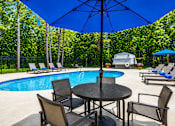 Thumbnail 6 of 9 - A pool area with a table and chairs and an umbrella.