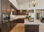 Thumbnail 10 of 21 - Clubhouse kitchen with dark wood cabinetry and granite island at Harper Ridge Apartments, Idaho, 83642