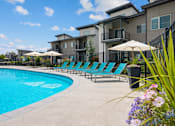 Thumbnail 2 of 21 - Resort style pool with lounge chairs and umbrellas at Harper Ridge Apartments, Meridian, ID 83642