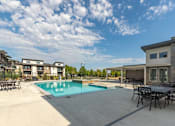 Thumbnail 22 of 29 - A swimming pool surrounded by a patio with chairs and a house in the background.