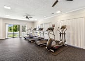 Thumbnail 20 of 28 - a gym with cardio machines and a ceiling fan