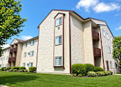 Thumbnail 2 of 2 - A large apartment building with a green lawn in front.