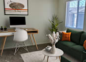 Thumbnail 4 of 16 - A modern living room with a green couch, a white desk, and a painting on the wall.