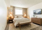 Thumbnail 10 of 11 - A bedroom with a large bed, a nightstand, and a painting on the wall.