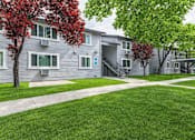 Thumbnail 3 of 11 - A tree with red leaves is in front of a grey building.