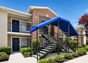Thumbnail 9 of 28 - A blue awning covers a staircase leading to a brick building.