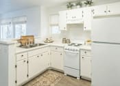 Thumbnail 17 of 28 - A white kitchen with a refrigerator, sink, and stove.