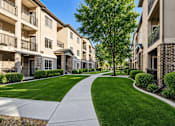 Thumbnail 2 of 17 - A row of apartment buildings with a sidewalk and green grass.