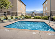 Thumbnail 8 of 17 - A swimming pool surrounded by lounge chairs and buildings in the background.