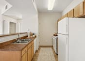 Thumbnail 16 of 21 - Galley kitchen with white appliances and wood cabinetry at Stetson Meadows Apartments, Colorado, 80922