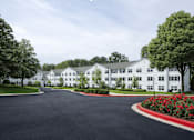 Thumbnail 3 of 10 - A white building with a black driveway in front.