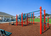 Thumbnail 11 of 20 - A playground with a red and blue structure and a green bench.